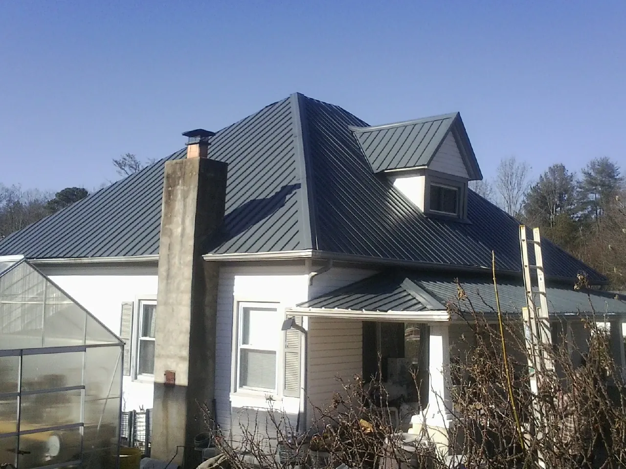 Dark blue standing seam metal roof on a white farmhouse with dormer — Slate & Tile Roof Repair by Roofing Brothers in Niwot