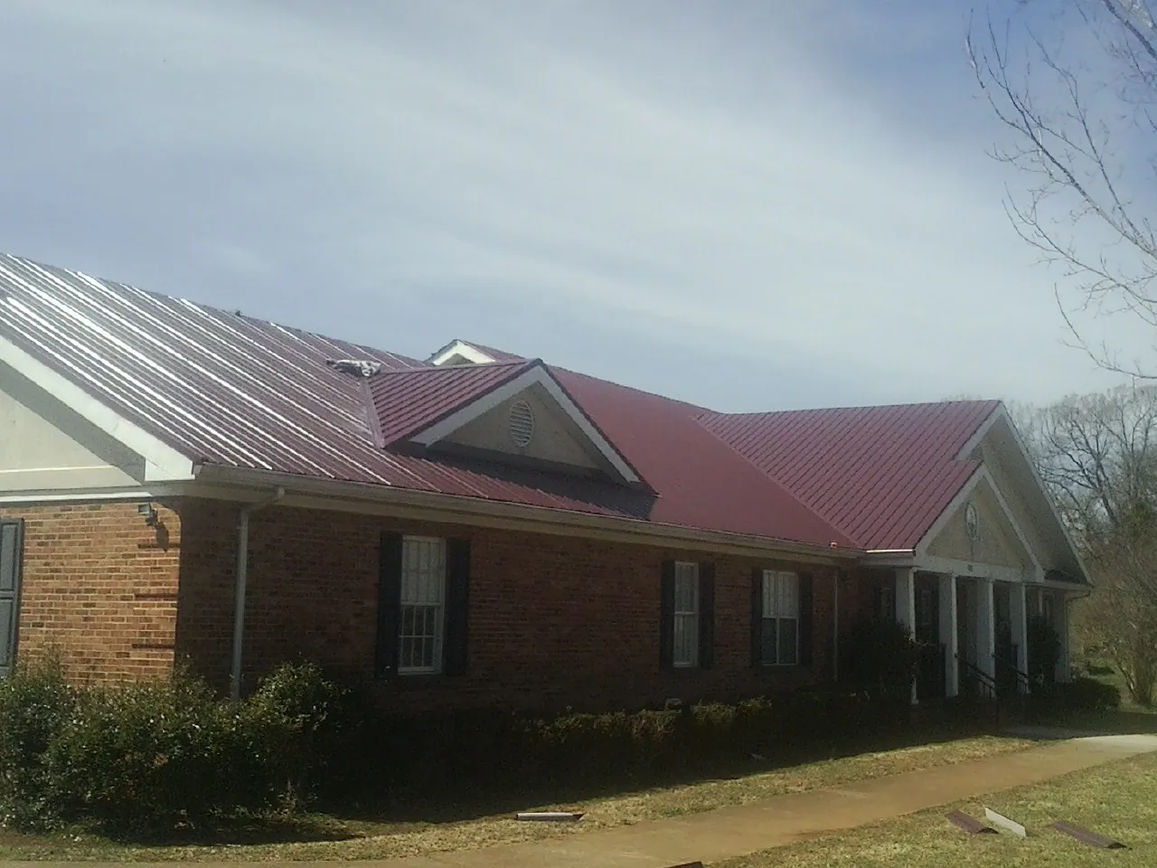 Red metal roof with gabled entries on a long brick building, from a Hail Damage Roof Repair job in Niwot