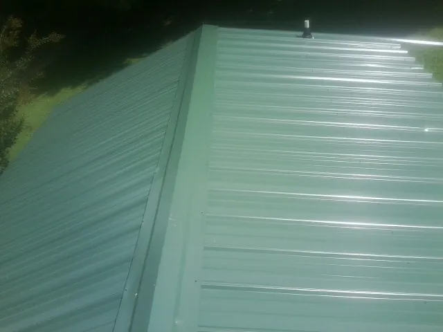 New green metal panels meeting at the ridge of a roof — Flat Roof Repair work by our crew in Niwot