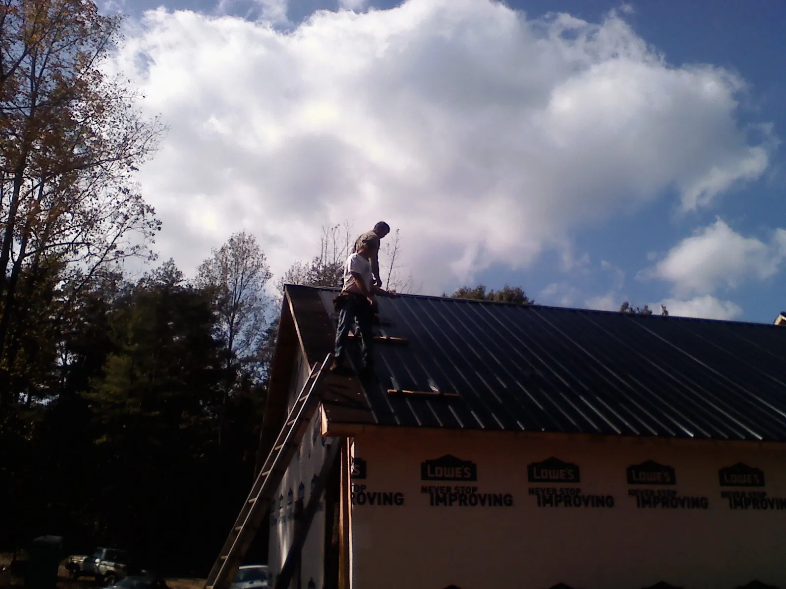 Roofer fastening dark metal panels high against a cloudy sky, from a Roof Inspection job in Niwot