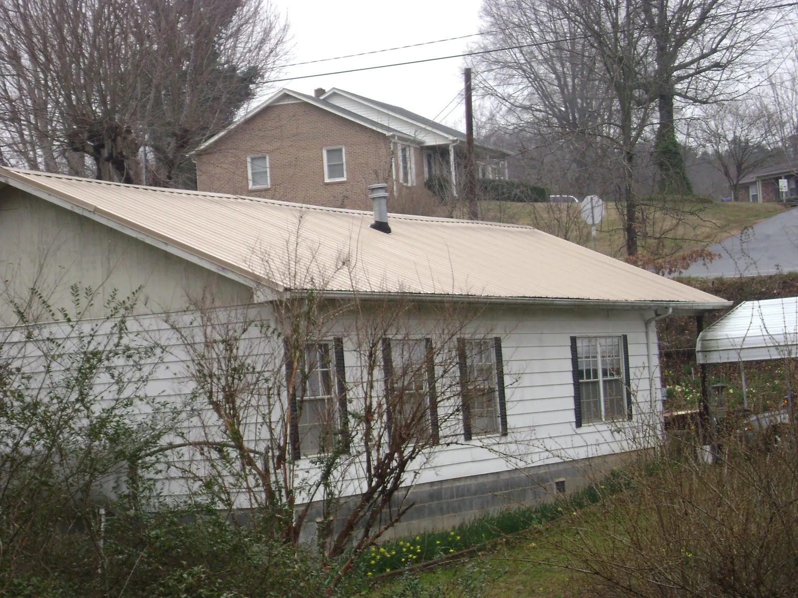 Tan metal roof on a white sided house set into a hillside — Commercial Roofing by Roofing Brothers in Niwot